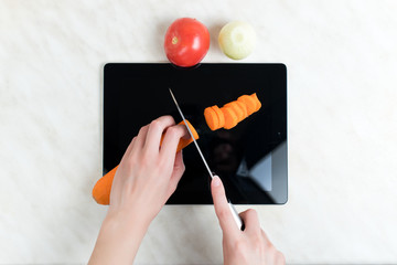 A woman cuts vegetables with a knife on an old graphics tablet