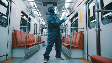 African man with protective suit , face shield, mask and gloves disinfecting interior of the train. Prevention of the spread in the public transport.