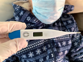 Hand in medical glove holds a digital thermometer. Sick male man patient on a background