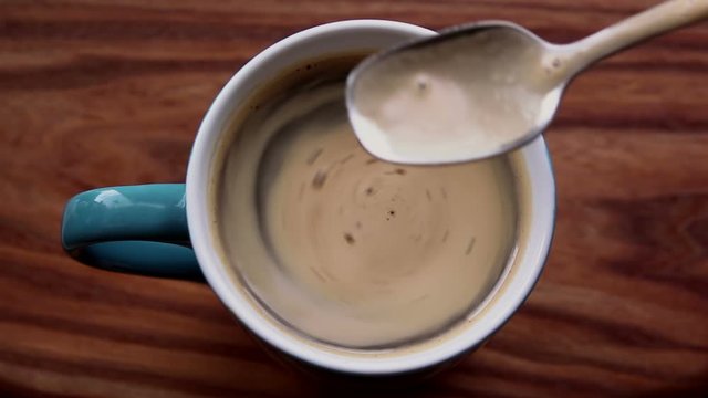 A man stirs sugar in a cup of aromatic coffee. A cup of aromatic coffee is placed on a wooden table. Man hands stir a coffee drink with a spoon. Invigorating coffee with delicious milk foam.