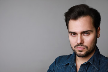 Portrait of 30-year-old man standing over grey background in denim shirt. Close up. Copy-space. Studio shot.