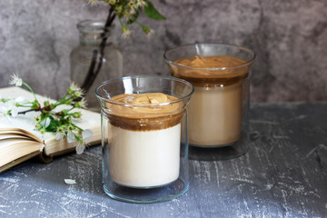Dalgona Coffee in transparent glasses, a book and flowers on a concrete table.