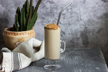 Dalgona Coffee in a transparent cup with a cocktail straw and cactus on a concrete table.