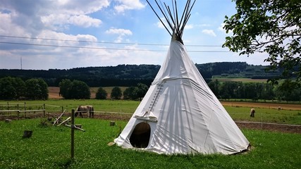 Indianer Zelt Tipi auf einer grünen Wiese mit blauem Himmel im Sommer.