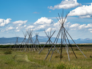 Nez Perce teepee frames with white billowing clouds and blue sky in background.