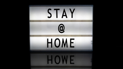 Stay @ home letters on a light box on reflective surface