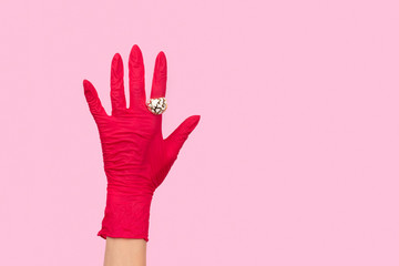 Womans hand in a rubber glove with golden ring on pink background