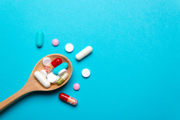 Wooden spoon with different pills, blue background
