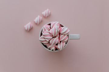 Marshmallows white and pink chewy candy over pink background, closeup. Sweet holiday food dessert in a cup close-up.