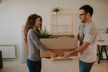 Fototapeta na wymiar Photo of attractive young couple carrying cardboard box together. Young couple is having fun while moving in to their new home.