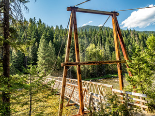 Fototapeta premium Wooden pedestrian bridge suspended over mountain stream