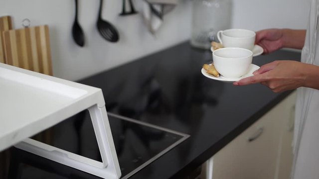 The girl puts two cups of coffee on a tray. Morning coffee. Coffee with cookies