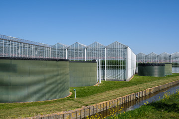 Fototapeta na wymiar Perspective view of a modern high tech industrial greenhouse with water tanks in front in the Netherlands