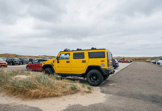 Overveen, Netherlands - Aug 16, 2019: Side view of luxury yellow hummer large SUV parked in the sand covered Dutch paid parking