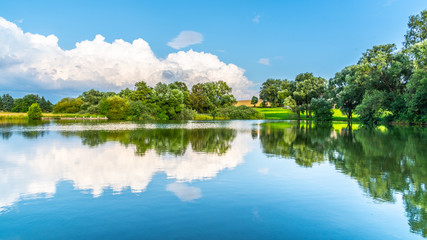 Fototapeta na wymiar Rural summer landscape reflected in the pond. Blue sky, white clouds and lush green trees