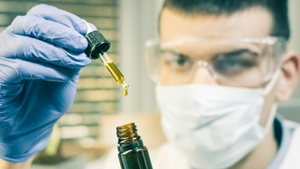 Examining cannabis cbd thc oil in medical scientist hands in pharmaceutical laboratory with mask...