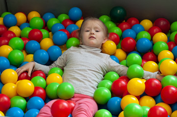 Happy little girl having fun in ball pit in kids indoor play center