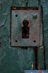 Close-up on old rusty metal lock. Green-painted key closure on a worn wooden door in a garden. Paint flaked.
