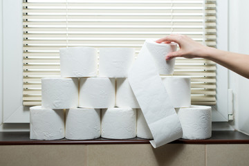 A hand takes a roll of toilet paper from the windowsill in the toilet
