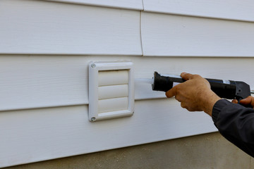 Laundry the white frame of a exhaust fan dryer fans with a silicone gun in apartment building trim