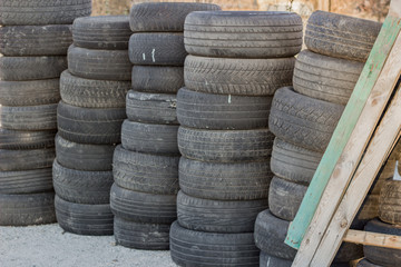 A stack of old rubber wheels lies on the street in several rows. Used black tires.