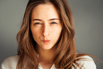 Naklejka premium Serious girl with a gaze and closed lips in a tube on a gray background, close-up. Nude makeup, without retouching.