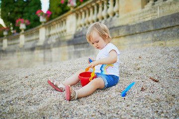 Little girl sitting on a large heap of stones and playing with pebbles