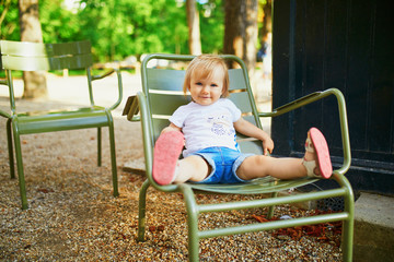 Fototapeta na wymiar Happy little girl sitting on green metal chair in Luxembourg garden of Paris