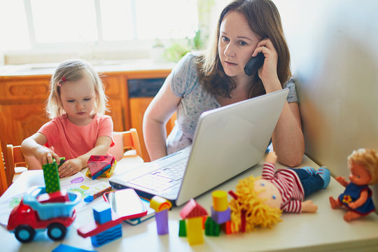 Exhausted And Stressed Mother Working From Home With Toddler