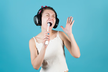 Fototapeta premium Girl in headphones sings in a toothbrush while brushing teeth on a blue background