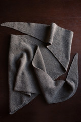 brown knitted triangular scarf lies on the table, table brown texture