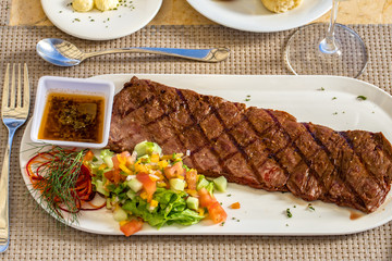 Churrasco beef meat with vegetables and sauce on a white plate, restaurant dish