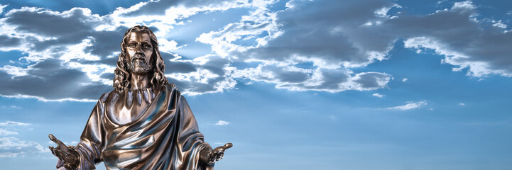 A bronze statue of a Jesus Christ with a dramatic sky