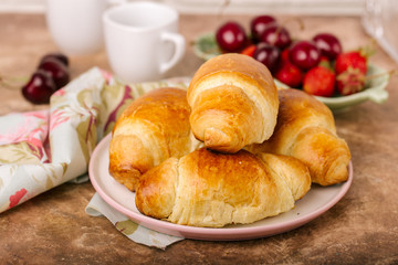 Freshly croissant on plate, fresh berries, cup of coffee, napkin, on marble texture background. Close up