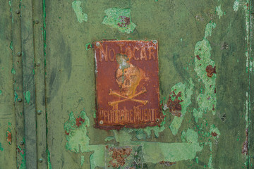 old rusty metal door painted green with a rusty red skull and crossbones danger sign
