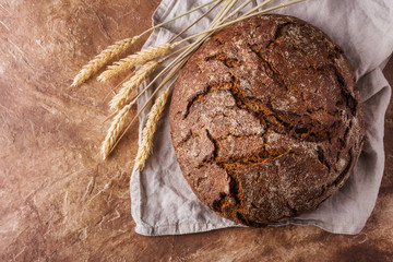 Freshly baked rye bread on cotton napkin, on brown table, space for text. Top view.
