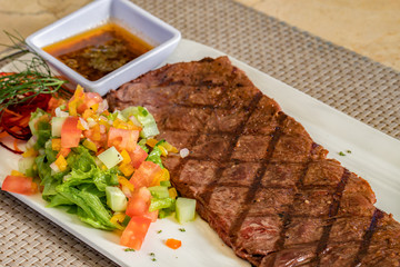 Churrasco beef meat with vegetables and sauce on a white plate, restaurant dish
