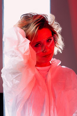 Portrait of a little girl doctor in glasses and gloves, in a protective suit. Cellophane background with red light. Art photography