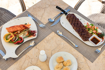 Salmon fillet with vegetables, churrasco beef meat with a green salad on a restaurant table