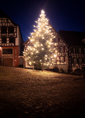 gran abeto de navidad por la noche iluminado de luces de color blanco en villa medieval