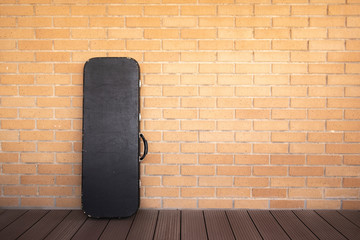 black electric guitar suitcase leaning against brick wall