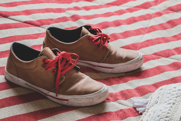 Pair of brown leather shoes with red laces on striped fabric background