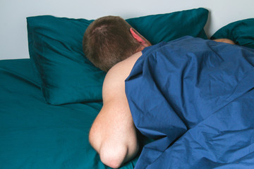 A man sleeps on his stomach in bed. Quarantine, self-isolation. Boredom, sleep, laziness, insomnia. Dark textile.