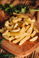 Tasty french fries on cutting board, on wooden table background with dill