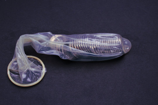 Metal coins in an unpacked condom on a black background, toned