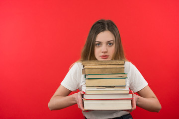 The girl in jeans and T-shirt stands and holds a book, she is tired and has no hunting learns, red background