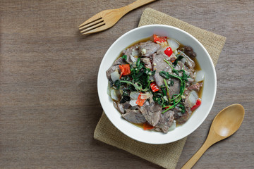 top view of stir fried stewed beef with holy basil in a ceramic bowl on wooden table. hot and spicy thai style food menu.
