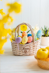 Multi-colored Easter eggs in a basket on a white wooden background