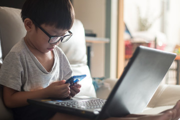 little boy Wear glass using laptop on sofa in home, work from home