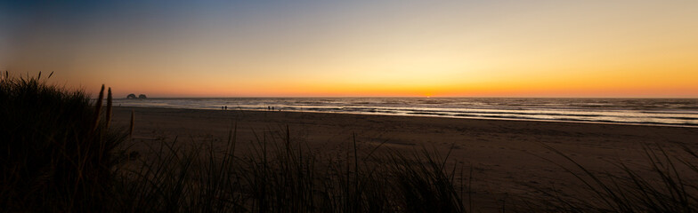 Panorama of the Oregon coast beach with a magnificent sunset and people taking a stroll.